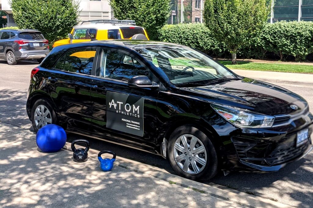 Atom Athletics personal training car parked on the street with gym equipment including a medicine ball and kettlebells.