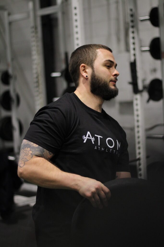 Personal trainer at Atom Athletics gym lifting a weight plate, preparing for strength training.