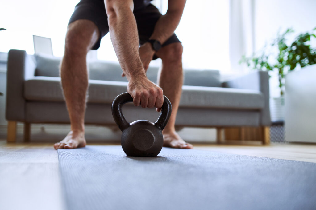 A close-up of a client reaching for a kettlebell on a workout mat in their living room during a session with an in home personal trainer in toronto.